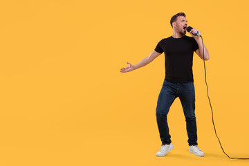 Handsome man with microphone singing on yellow background. Space for text - Powered by Adobe