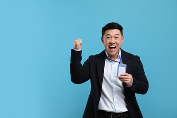 Excited asian man with vip pass badge on light blue background. Space for text