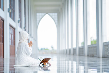 The image of an Asian Muslim woman in the Islamic religion in hijab in white color. reading the Quran, Koran Staying in a beautiful mosque, Arabic word translation: The Holy Al Quran.