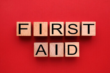 Words First Aid made of wooden cubes on red background, flat lay