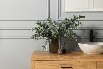 Eucalyptus branches, candle and aroma sticks near vessel sink on bathroom vanity. Interior design