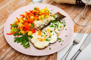 Closeup of sliced fried codfish served with potatoes and carrots at plate