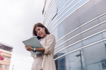 Charming Asian woman with a smile standing holding papers and mobile phone at the office.