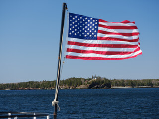 The American flag at the rear of the ferry to Vinalhaven island with the Owls Head Lighthouse on the cliffs in the background