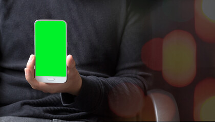 Casual businessman working showing a green chroma screen mobile phone, presenting ideas, apps, a website, an advertisement or a call with bokeh lights in the foreground.