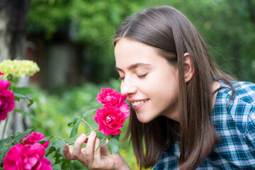 Naklejka premium Beautiful girl smelling a rose flower in spring park. Young woman in flowering garden with roses. Beauty model with spring flowers. Happy spring. Pretty woman enjoying smell flowers in spring park.