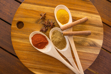 Spices in three wooden spoons with herbs and spices on a round wooden background