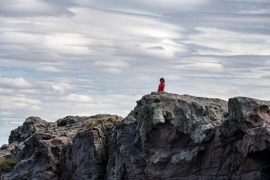 Senior woman looks at the landscape from a cliff with lenticular clouds in the background in Puerto Deseado, Santa Cruz, Argentina.