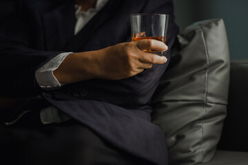 Businessman in black suit holding glass of whiskey Celebrate company success close-up