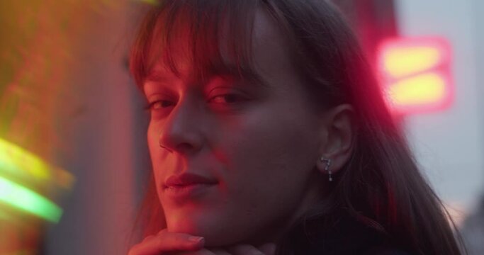 young woman, girl, staring into lens, gazing, red light, blurry lights, dawn, pretty mysterious look, earring, beautiful face, cinematic close-up shot.