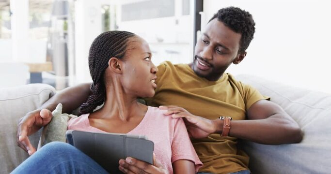 Happy african american couple using tablet and talking on couch at home, in slow motion