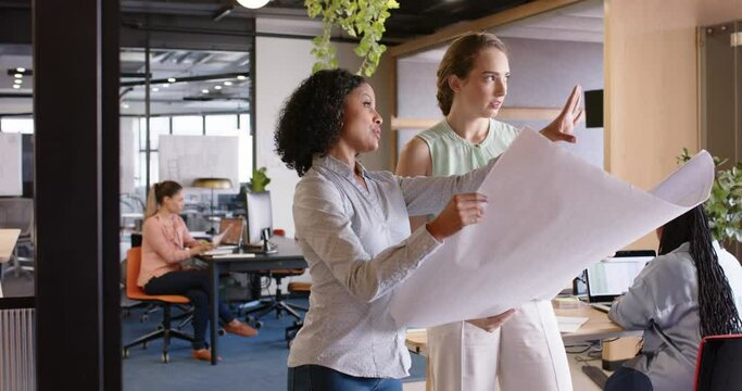 Diverse female architects discussing work and looking at blueprints at office, in slow motion