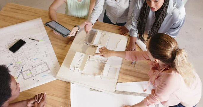 Diverse female architects discussing architectural model and blueprints at work, in slow motion