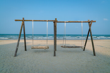 Swing made of wood and timber with two seats on the beach. Sea with horizon background. Travel or vacation concept.
