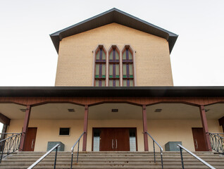 vue d'en bas d'une bâtisse beige au toit en angle avec des fenêtres verticales et une entrées sous un toit