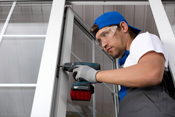 Serious man in uniform and a screwdriver fixes the plastic door to the base. Professional installation of a plastic door by an experienced craftsman