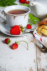 Delicious breakfast of tea, fresh bread rolls with sesame seeds and strawberries. On the background of an old white table. Rural motive.