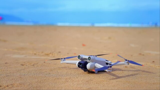 Drone starting flight on the beach. Drone starting engine motor and propellers to take off flight. Blurry beach in the background. Grey drone lifting into the air.
