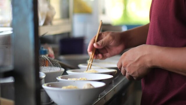 Preparing chicken noodles. View of a penjual mie ayam bakso or meatball chicken noodle seller who is making chicken noodles for the buyer. Selective focus. 