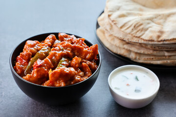 Schezwan Chicken or Dragon Chicken in black bowl at dark slate background. Szechuan Chicken is popular indo-chinese spicy dish with chilli peppers chicken and vegetables.