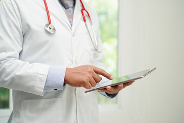 Asian man doctor using tablet computer to reading patient report, check up and search for solve...