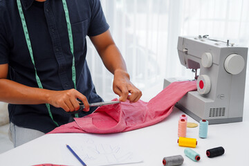 A young Asian male cropped an image of a t-shirt cut by scissors at the workbench