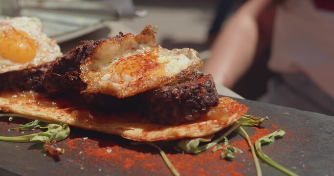 Close up shot of spanish tapas of morcilla blood sausage with egg toast on display on a restaurant table on a sunny day.