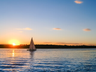 Golden glow of sun on horizon with yacht in silhouette sailing by