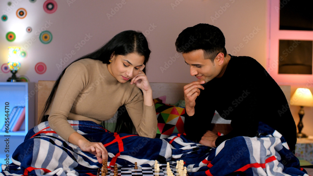 Wall mural A modern Indian couple playing a game of chess together at home - a boardgame. A healthy and happy family playing competitive chess - strategy  thought process  skillful