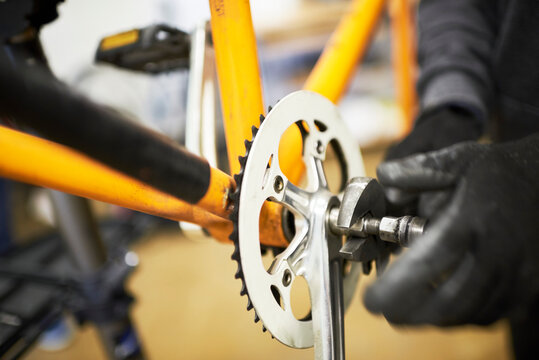 Maintenance of a bicycle: hands of an unrecognizable person using gloves disassembling the pedals of an orange bike with a wrench tool.