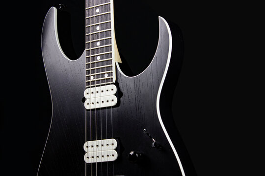 black electric guitar body with strings and frets with pick up on black background