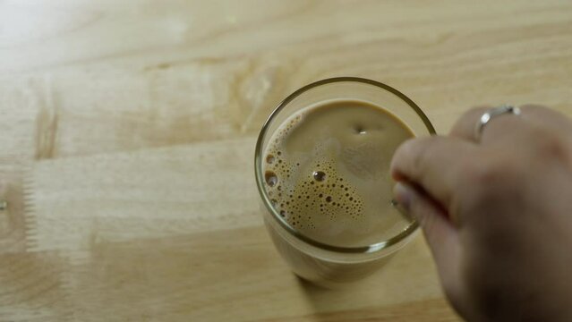 Top view of Person hand steering coffee in a cup with spoon. Breakfast morning of a cup hot black coffee on wooden background. footage b-roll scene 4k. home making coffee.