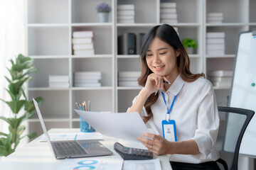 Beautiful young female manager or company worker holding accounting documents, checking financial data or marketing reports working in office with laptop. Accountant consults on some document.