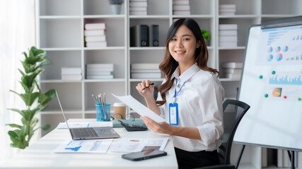 Beautiful young female manager or company worker holding accounting documents, checking financial data or marketing reports working in office with laptop. Accountant consults on some document.