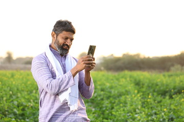 Happy Rural Indian bearded farmer is using his mobile phone or smart phone for text messaging while...