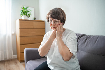 Hurt senior woman in glasses feel stressed suffering from severe toothache at home. Unhappy aged...