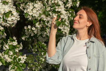 A beautiful red-haired woman in jeans and a white T-shirt holds a branch, studded with white...