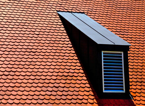 Sloped Red Clay Tile Roof With Round Beaver Tail Edge. Black Metal Plated Roof Dormer With White Metal Louver. Modern Home Building Materials Concept. Residential Building Construction.