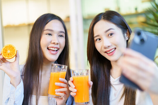 Asian women enjoying eating a breakfast and drinking organic orange juice together in the dining room and using smartphone taking a selfie.