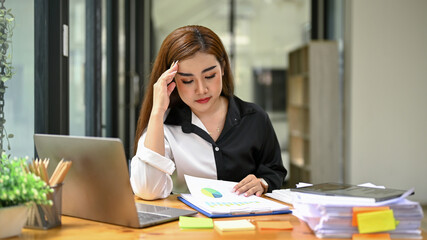 Stressed Asian businesswoman focuses on reviewing accounting reports