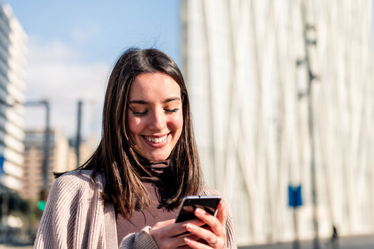 young woman smiling happy while texting on her mobile phone, concept of modern lifestyle and technology of communication, copy space for text