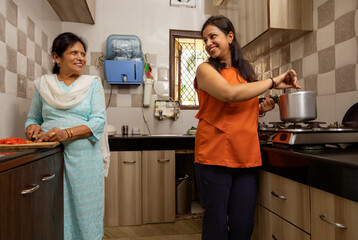 Mother-in-law helping her daughter-in-law in cooking in the kitchen