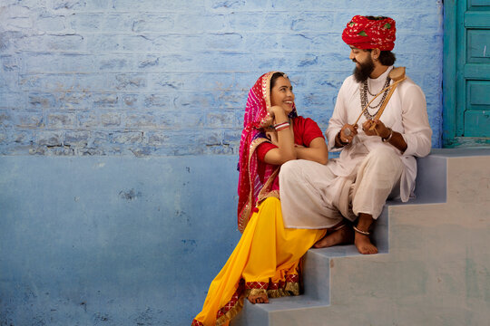 Rajasthani couple sitting on stairs sharing a light moment, as the husband plays ektara