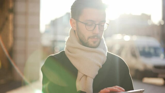 Stylish serious man walk down street in city with tablet in hands typing message, looking at screen, working or checking email. Entrepreneur, workaholic busy person, businessman, multitasking concept.