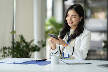 Confident businesswoman is using smartphone to contact clients to discuss working with financial documents, marketing, earnings in office.