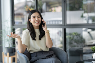 Fototapeta premium Young attractive Asian woman or businesswoman using a mobile phone. Communicate on the web, work, talk and learn online. Business management while sitting on sofa chair.