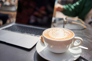 A cup of cappuccino and a laptop on the table in a coffee shop. Workplace in a coffee shop in the morning. coffee break.