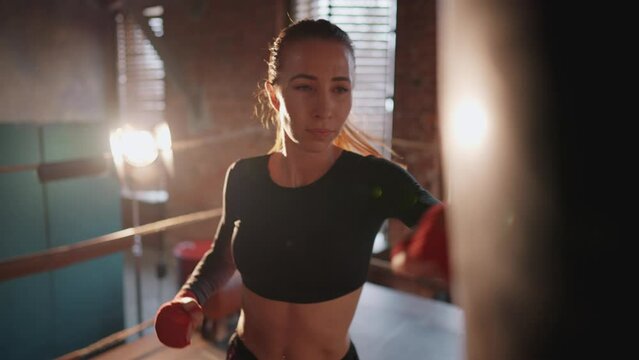 Young strong woman boxer in sportswear gives punches by hans on boxing ring. Training, workout and professional sport concept. Self-defence, girls power, womans power and prepares to fight, feminism.