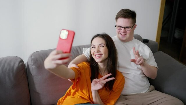 Down Syndrome man sitting on sofa with a girl, they make selfie together
