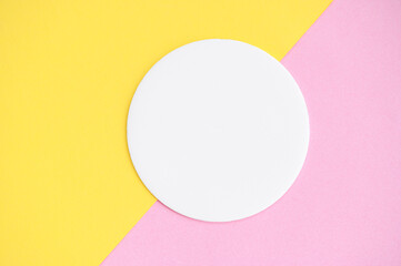 Empty round geometric shape in white color on pink and yellow colored paper background. Top view mockup for product demonstration